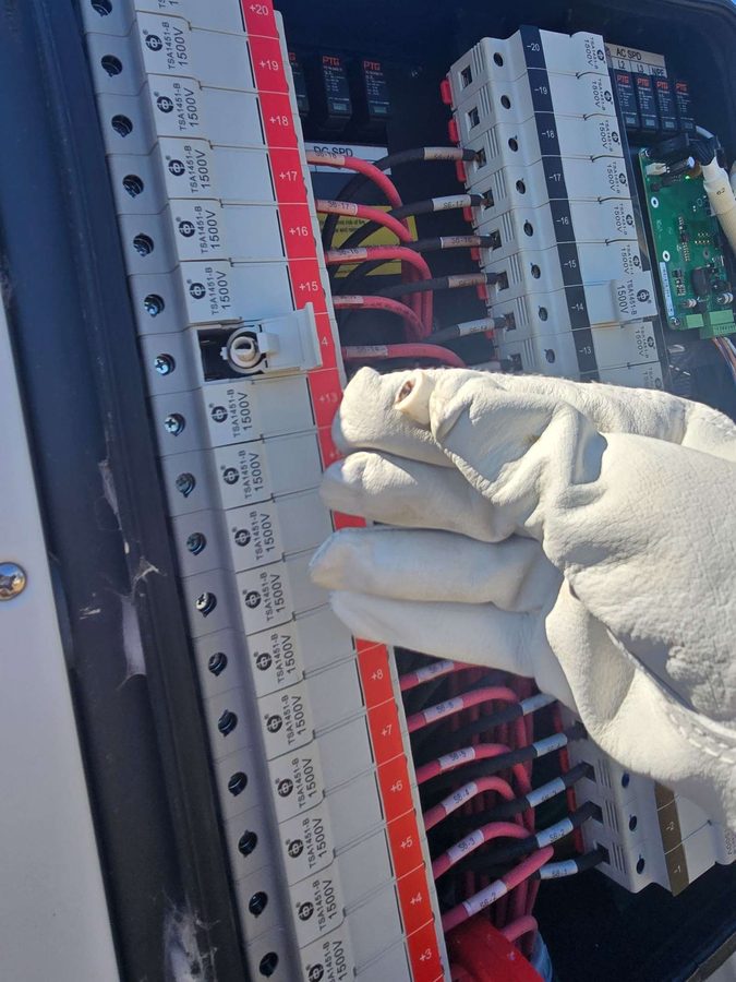 Gloved hand checking string fuses inside an inverter